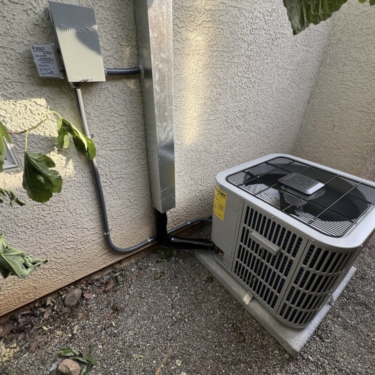 New AC condenser with disconnect box and line set installed against stucco wall