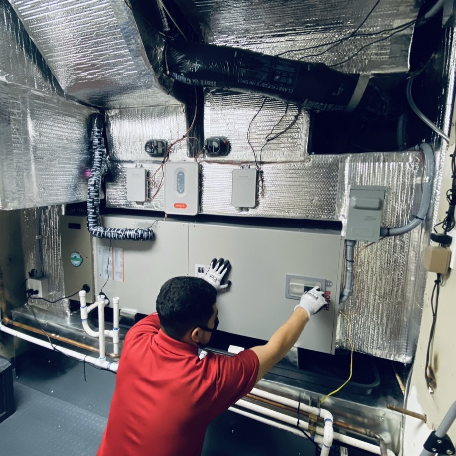 HVAC technician servicing commercial rooftop unit with manifold gauges and insulated ductwork
